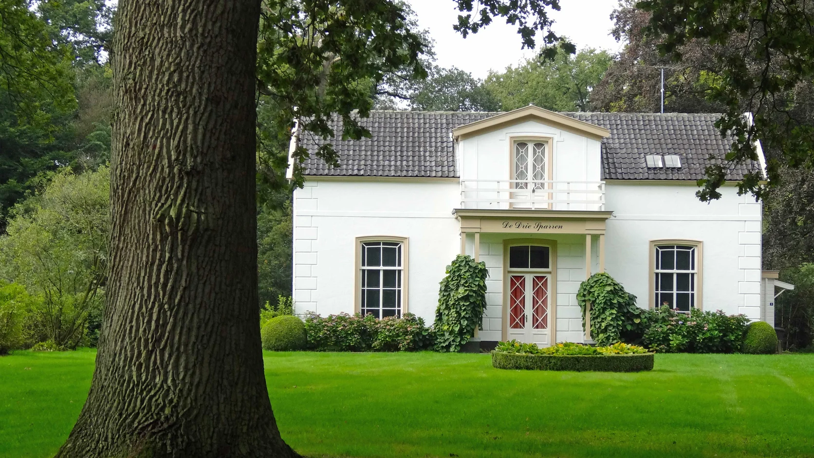 Tuinmanswoning op landgoed Eerde bij Ommen tussen hoge bomen en groen gazon.